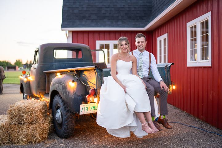 Bride and groom on a vintage truck by a red barn at golden hour