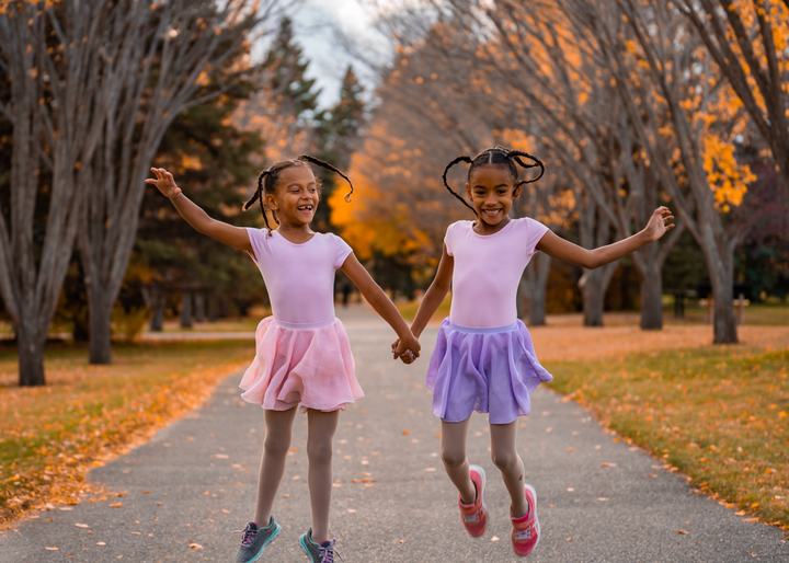 Two sisters in tutus skipping down an autumn path